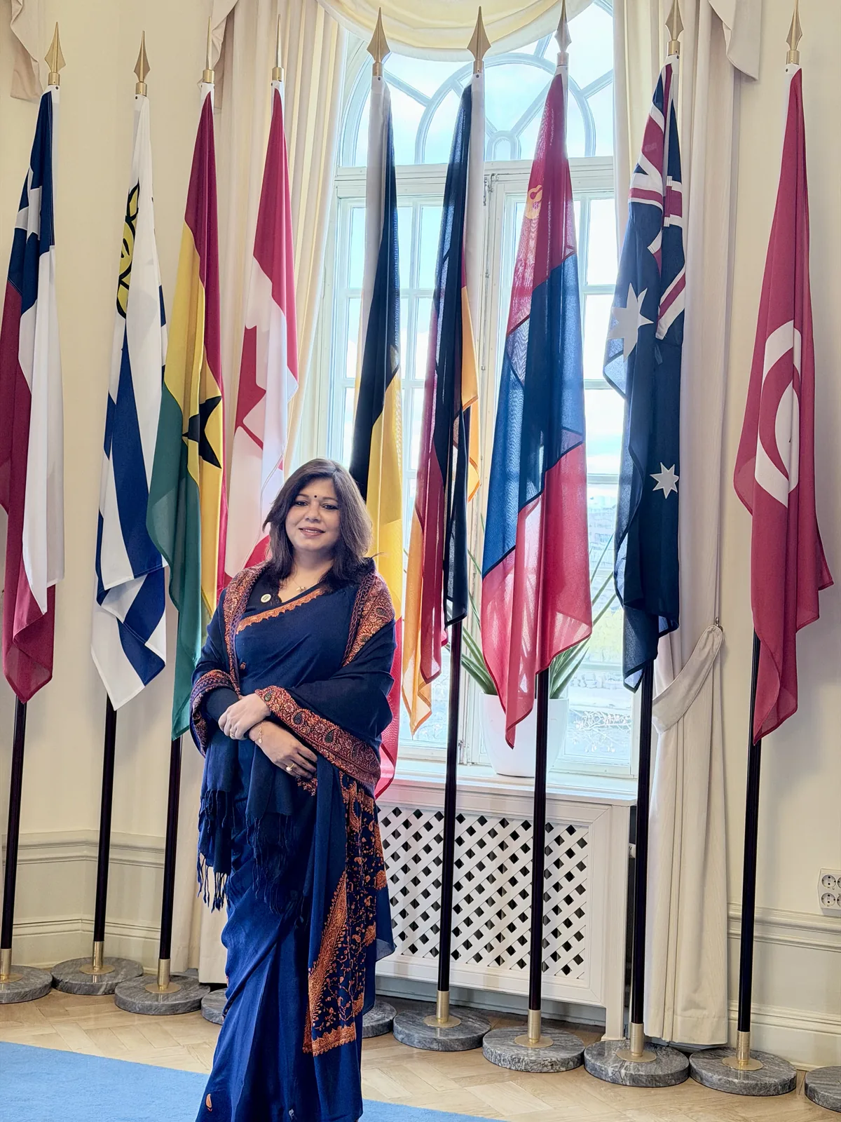Shubhra Saxena at an international gathering, standing among the flags of participating nations