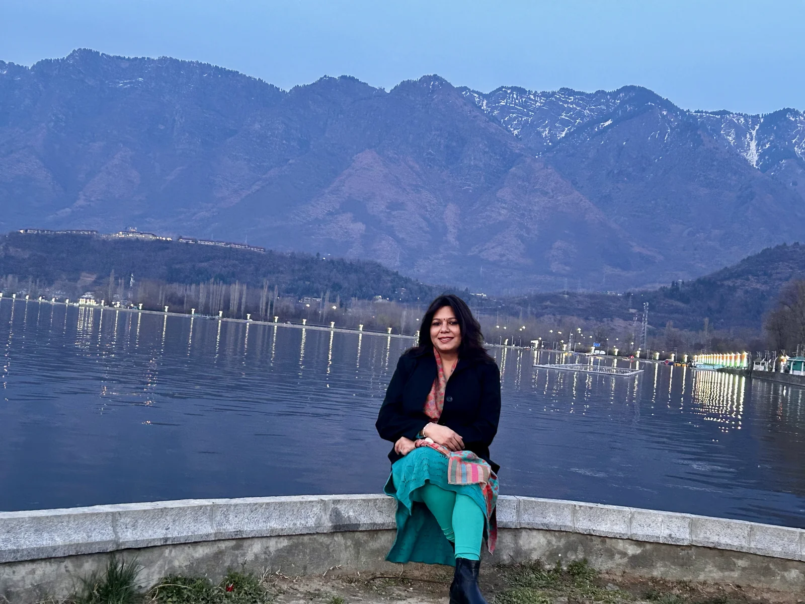 Shubhra Saxena seated beside a lake, with snow-capped mountains in the background